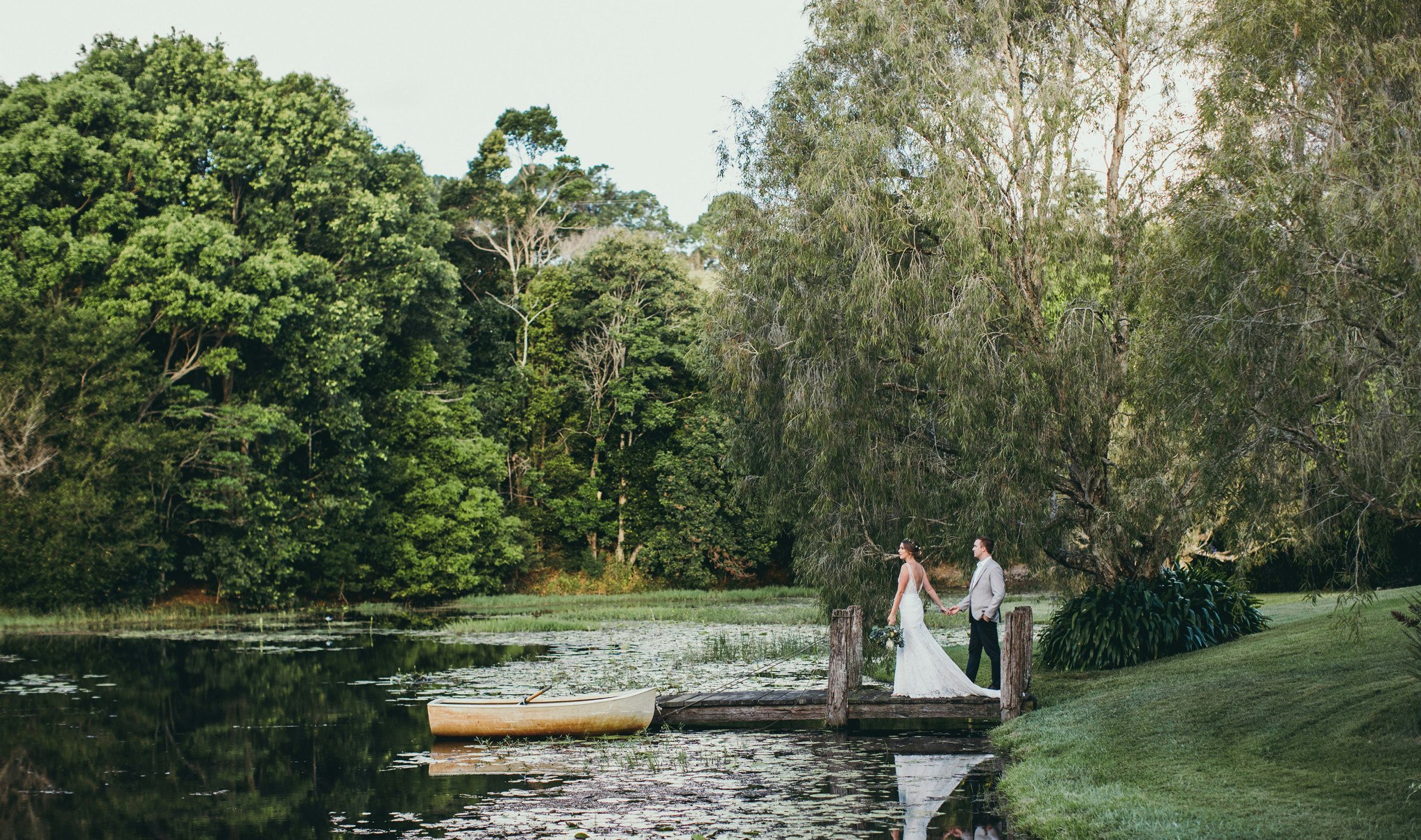 Wedding couple walking onto jetty towards a docked boat.